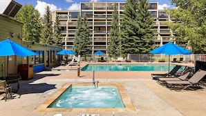 Área de piscina com espreguiçadeiras e guarda-sóis, cercada por um edifício com várias varandas.