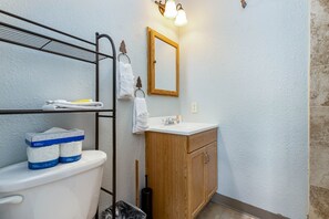 Une salle de bain comprenant des toilettes, un meuble en bois, un miroir et une étagère avec des serviettes et du papier toilette.