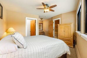 Une chambre à coucher avec un lit, un ventilateur de plafond, une armoire en bois et une fenêtre.