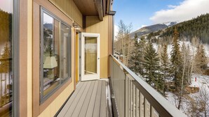 A wooden balcony with large windows overlooking a snowy landscape and forested mountains. - 2797 Slopeside Condo (Keystone)