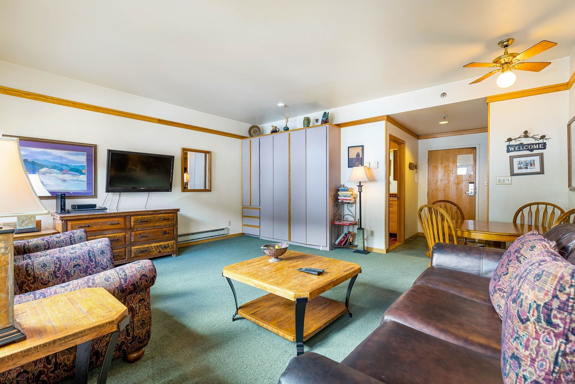 A living room with a sofa, a wooden coffee table, a TV, a cabinet, and a dining area with a table and chairs.