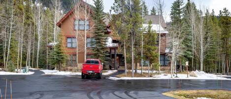 A lodge with a wooden exterior, a red truck parked in front, surrounded by trees and a mountain in the background.