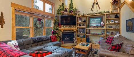 A cozy living room with a fireplace, a large window, and a Christmas tree.