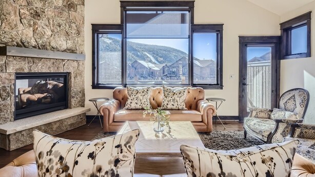 Un salon avec un mur en pierre, une cheminée, une grande fenêtre donnant sur les montagnes et un coin salon confortable.