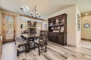 Enjoy meals in this cozy dining area with a large table and comfortable chairs, a stone fireplace, and a wooden cabinet for storage.