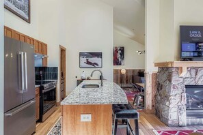 A modern kitchen with granite countertops, stainless steel appliances, and a stone fireplace. - 2301 Red Hawk Lodge 2 Bedroom Condo (Keystone)