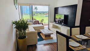 Uma sala de estar com sofá, mesa de centro, televisão e um canto de jantar com cadeiras e mesa.