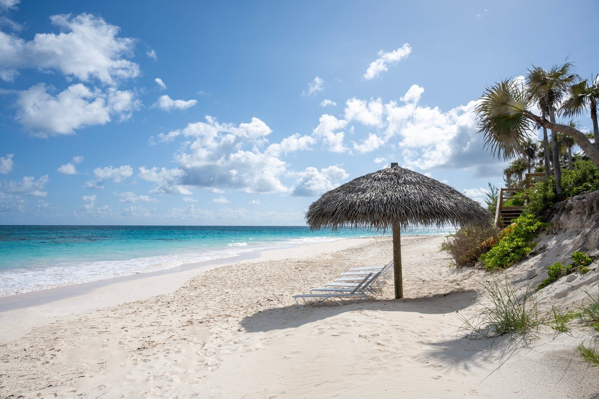 Ein Strand mit einem Reetdachschirm, weißem Sand und klarem, blauem Wasser.