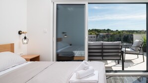 Ein modernes Hotelzimmer mit einem großen Bett, einem Nachttisch, einer Wandlampe und Blick auf einen Balkon mit einem Stuhl und einer Pflanze.