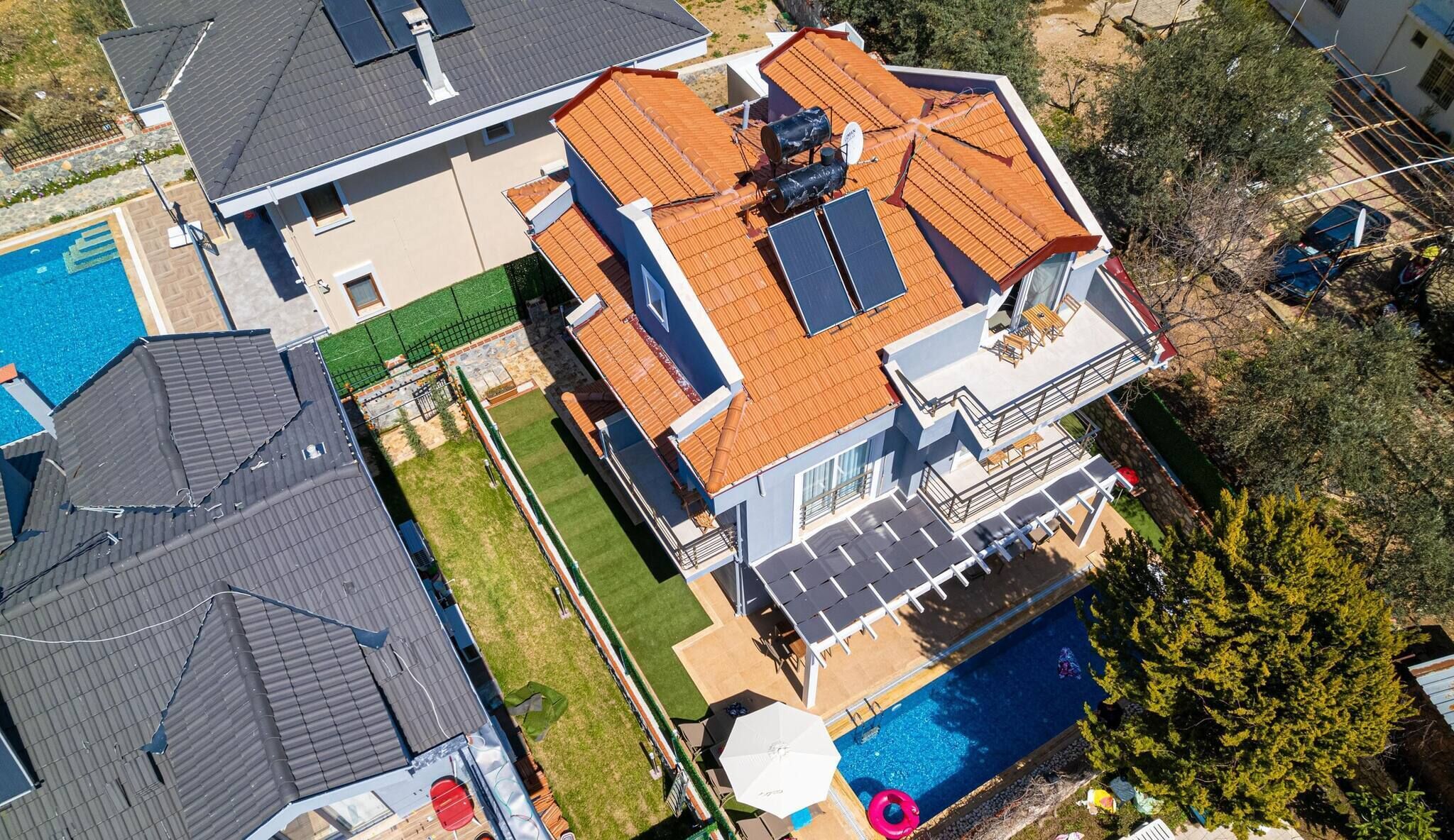 A multi-story house with a swimming pool, solar panels, and a fenced backyard.
