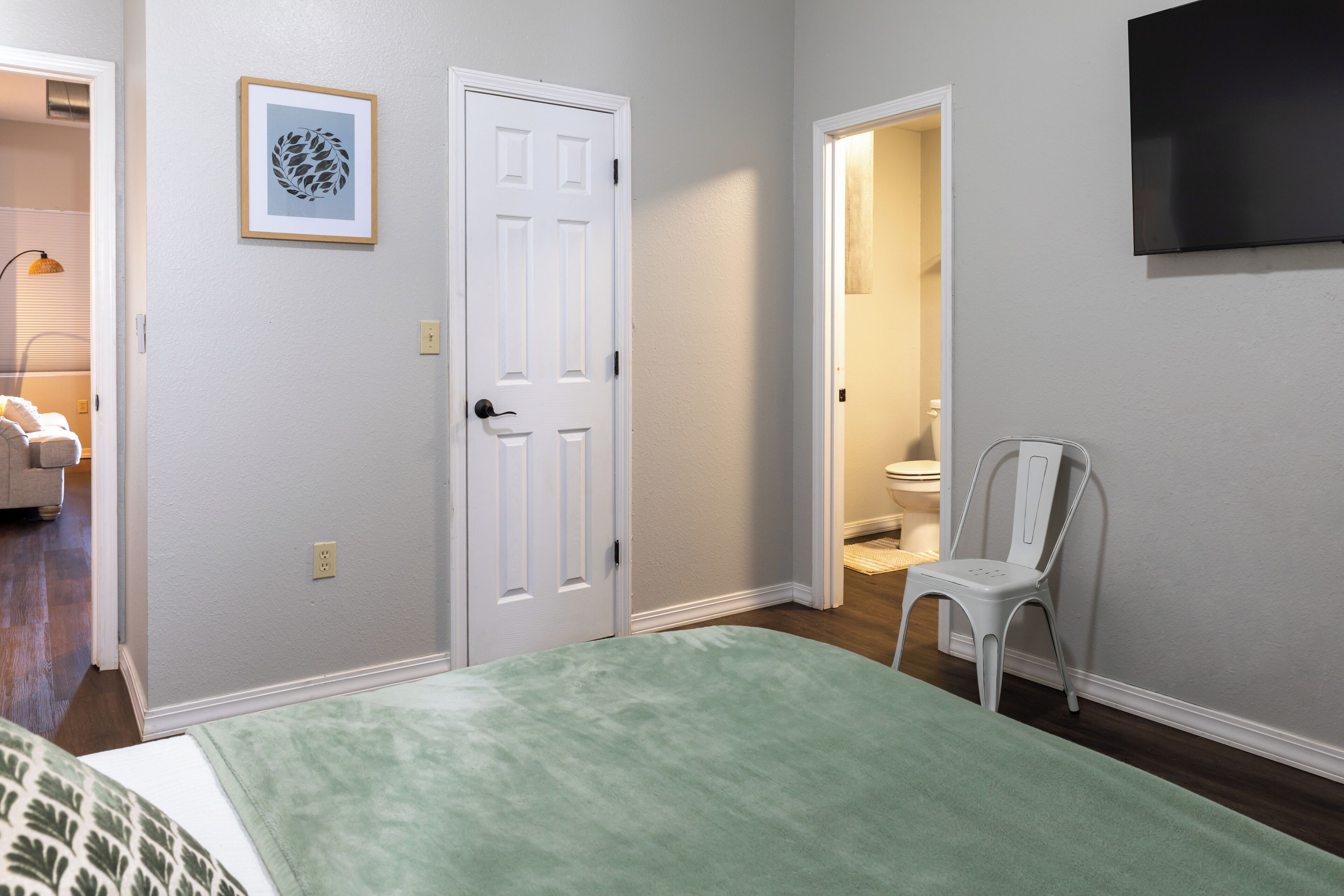A bedroom with a bed, a chair, a door, and a TV on the wall.
