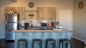 A modern kitchen with a central island, bar stools, stainless steel appliances, and wooden cabinetry.