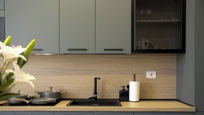 A modern kitchen with grey cabinets, a wooden countertop, a black sink, and a vase with white flowers.