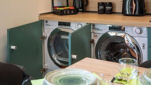 A compact laundry area with two washing machines, a tea box, and a coffee maker.