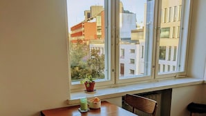 Un área de comedor con una mesa y sillas de madera, una ventana con vistas a edificios y una pequeña planta en maceta en el alféizar.