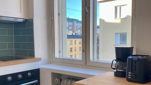 Una cocina con horno empotrado, refrigerador y ventana con vista a una zona residencial.