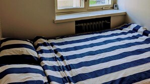 Un dormitorio con ventana, radiador y edredón a rayas.