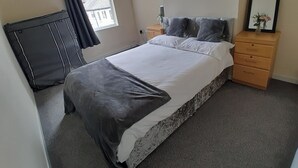 Un dormitorio con cama, cómoda, espejo y radiador.