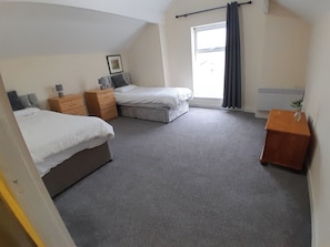 A bedroom with two beds, a dresser, a bedside table, and a window with curtains. - Blackpool - 2-beds - Sleeps 5 - Pet Friendly (Lytham St. Anne's)