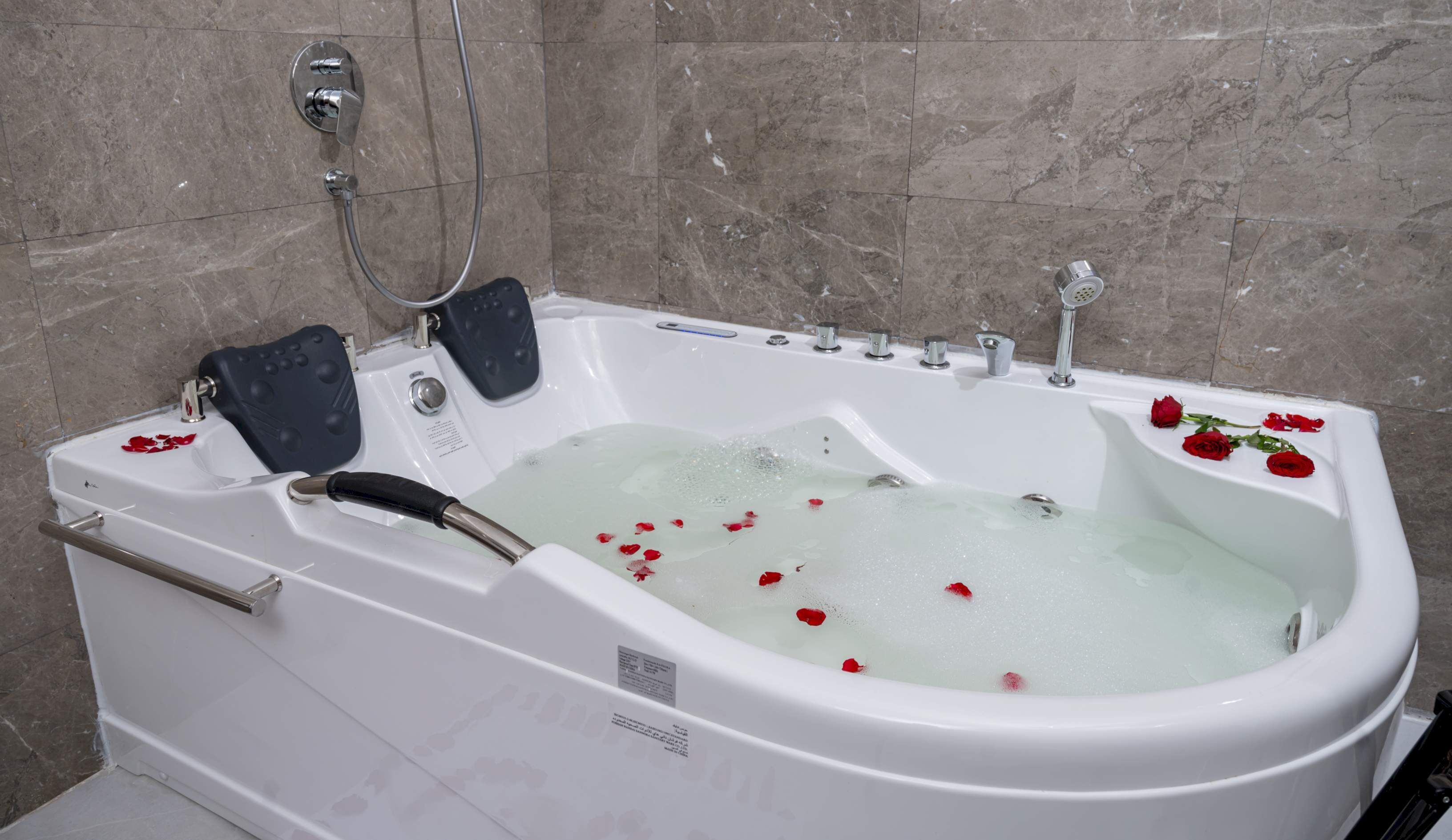 Een wit bad met rozenblaadjes in het water, een handdouche en een handmassageapparaat.
