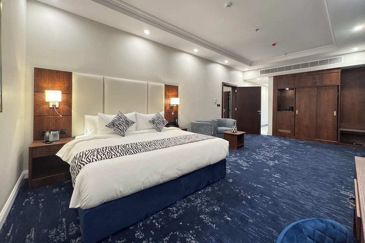 Habitación de hotel con una cama grande, un escritorio, una silla, un armario y una alfombra azul.