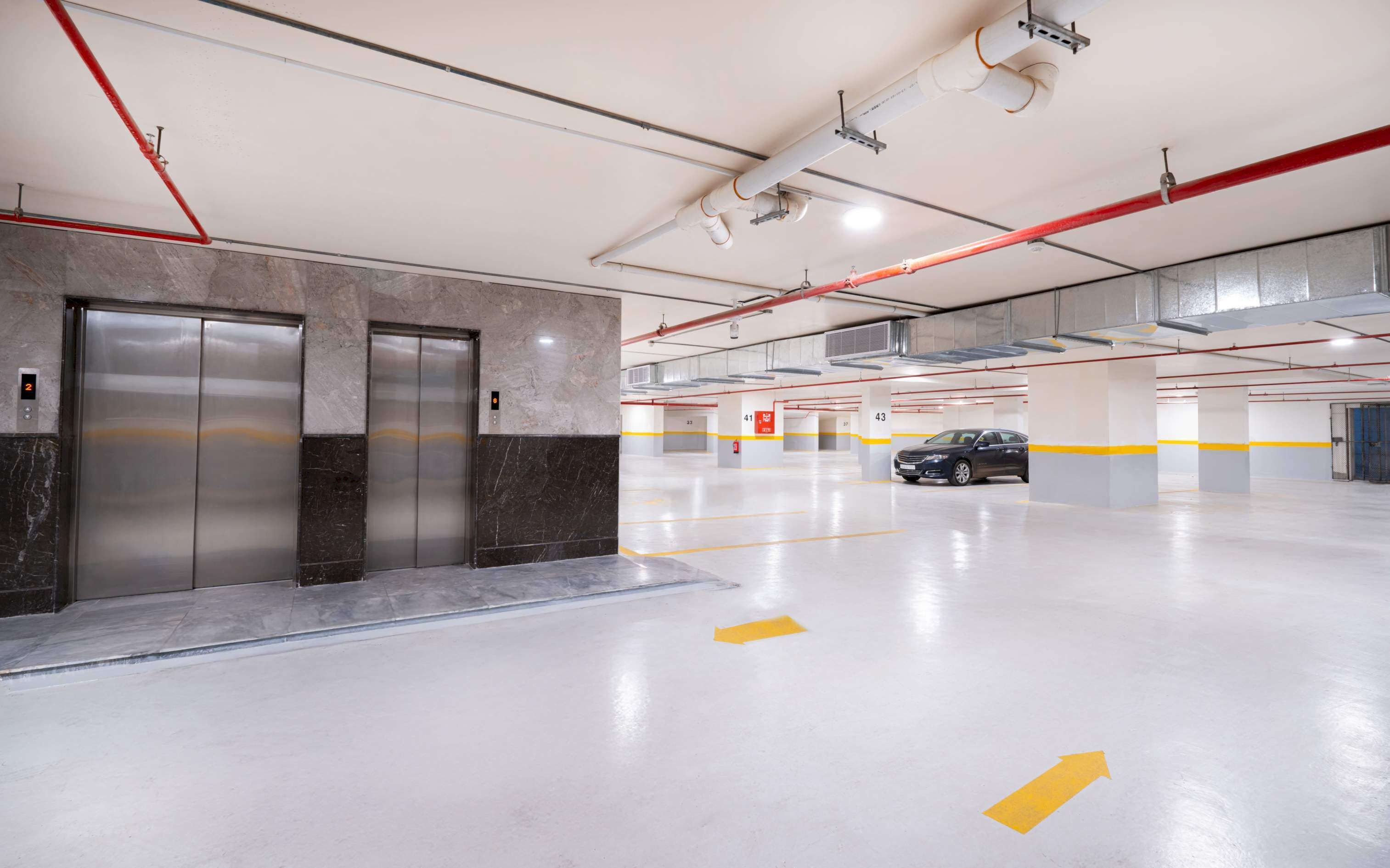A multi-level parking garage with a car in the distance, elevators, and clear directional arrows on the floor.