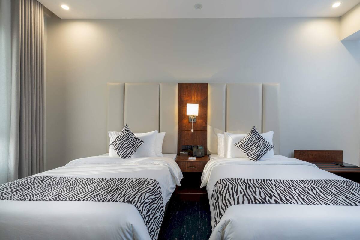 Una habitación de hotel con dos camas, una mesita de noche, una lámpara y un cabecero de madera.
