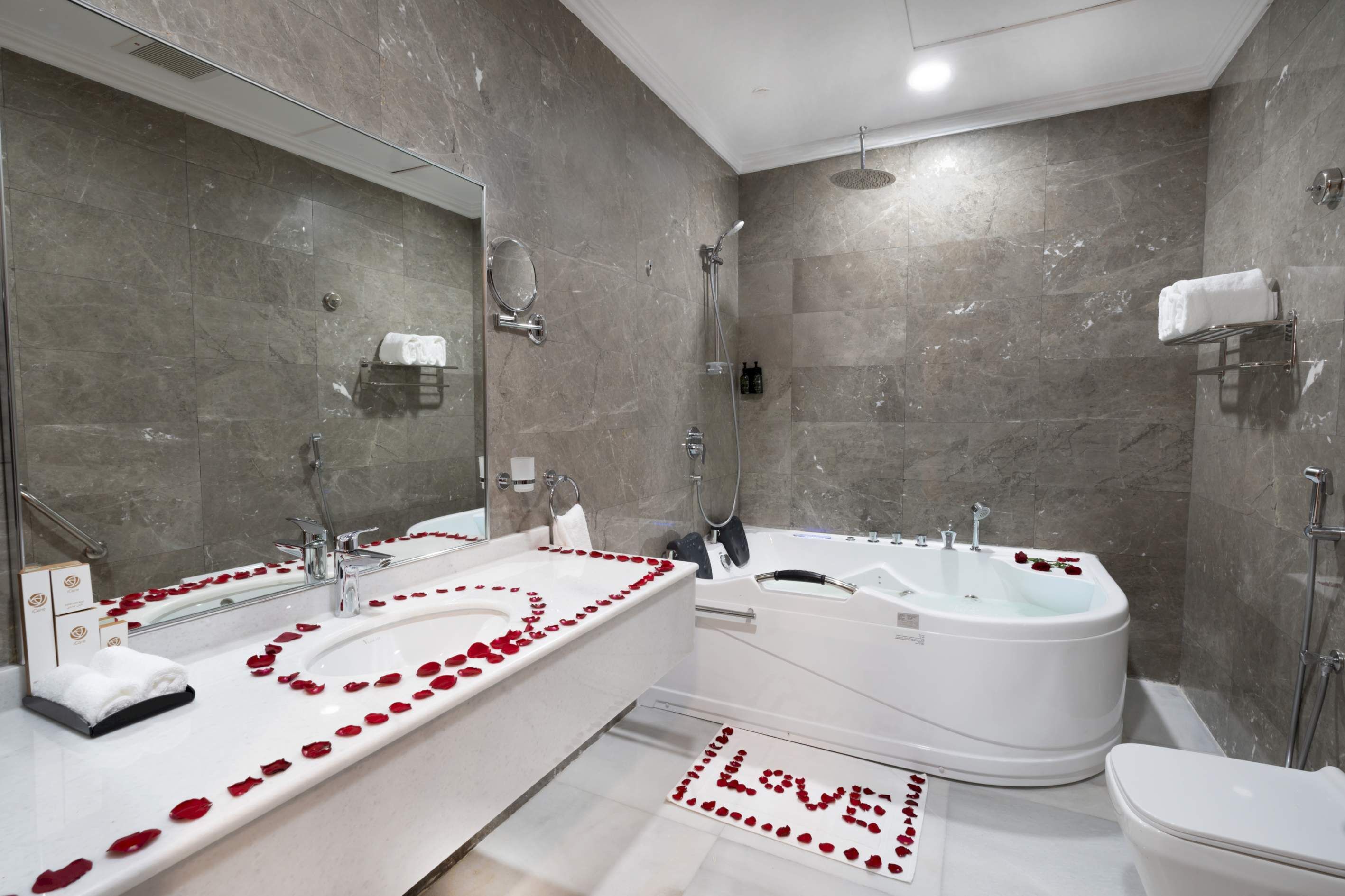 A modern bathroom with a large mirror, two sinks, a bathtub, and a toilet.