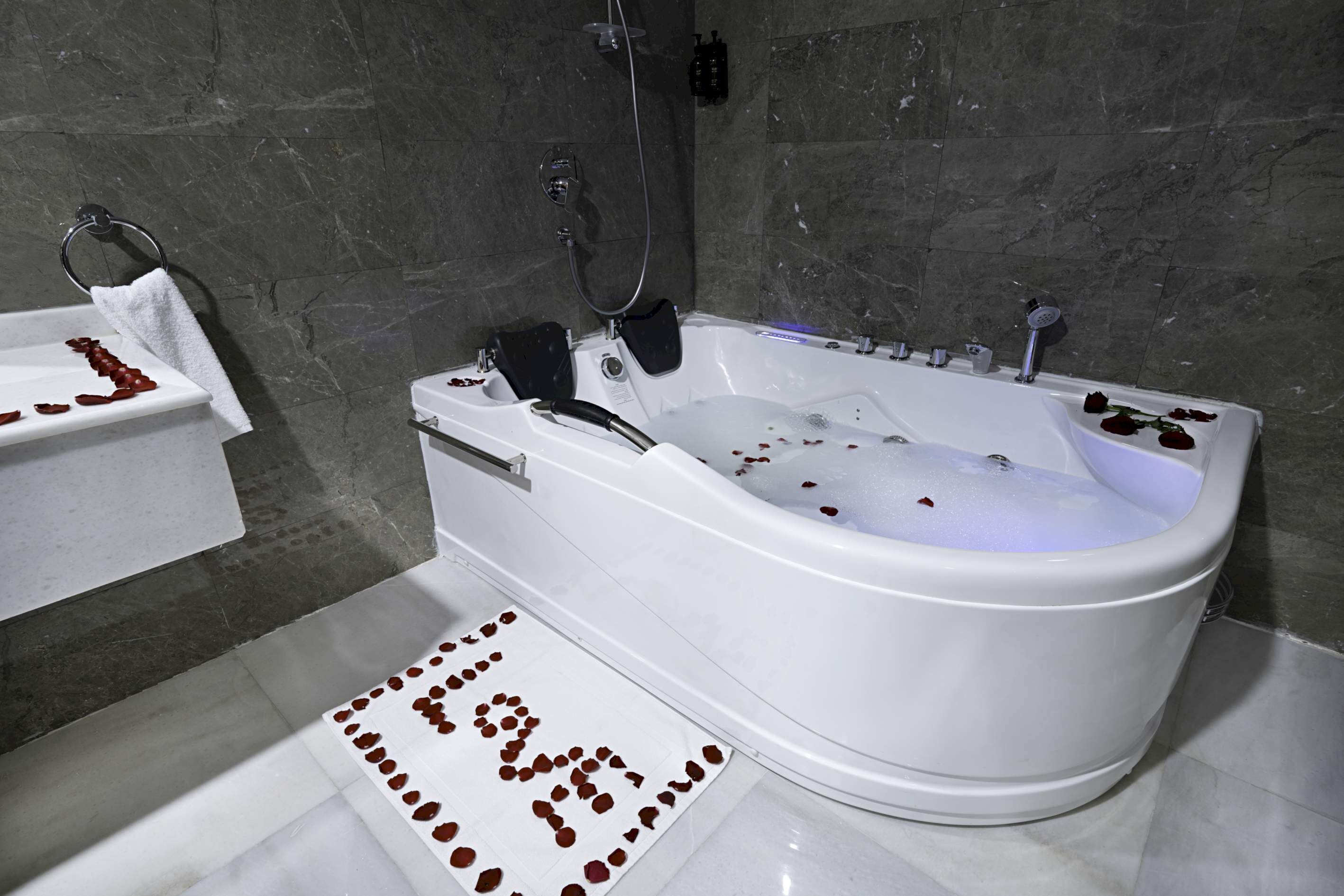 A modern bathroom with a freestanding bathtub, a towel rack, and a decorative arrangement of rose petals on the floor.