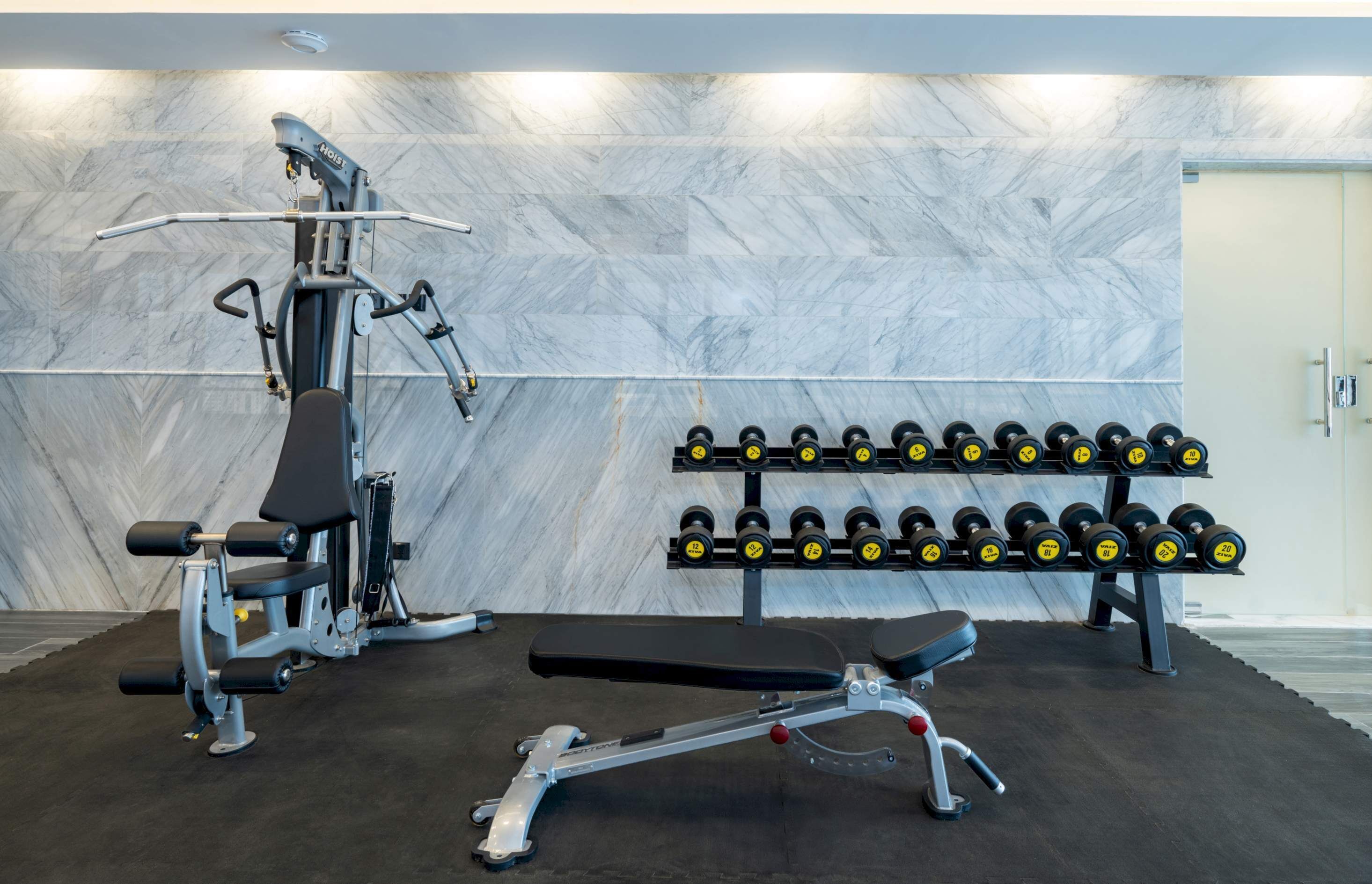 Une salle de sport équipée d’un rameur, d’un banc de développé couché, d’haltères et d’un mur au motif de marbre.