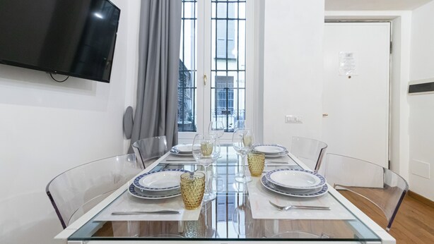 A dining area with a glass table, clear chairs, and plates with blue patterns.