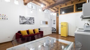 A compact living space with a red sofa, a glass dining table, a yellow refrigerator, and a white cabinet.