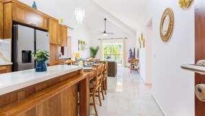 Eine moderne Küche mit Holzausstattung, einem Edelstahlkühlschrank, einer weißen Arbeitsplatte und einem Essbereich mit Holztischen und -stühlen.