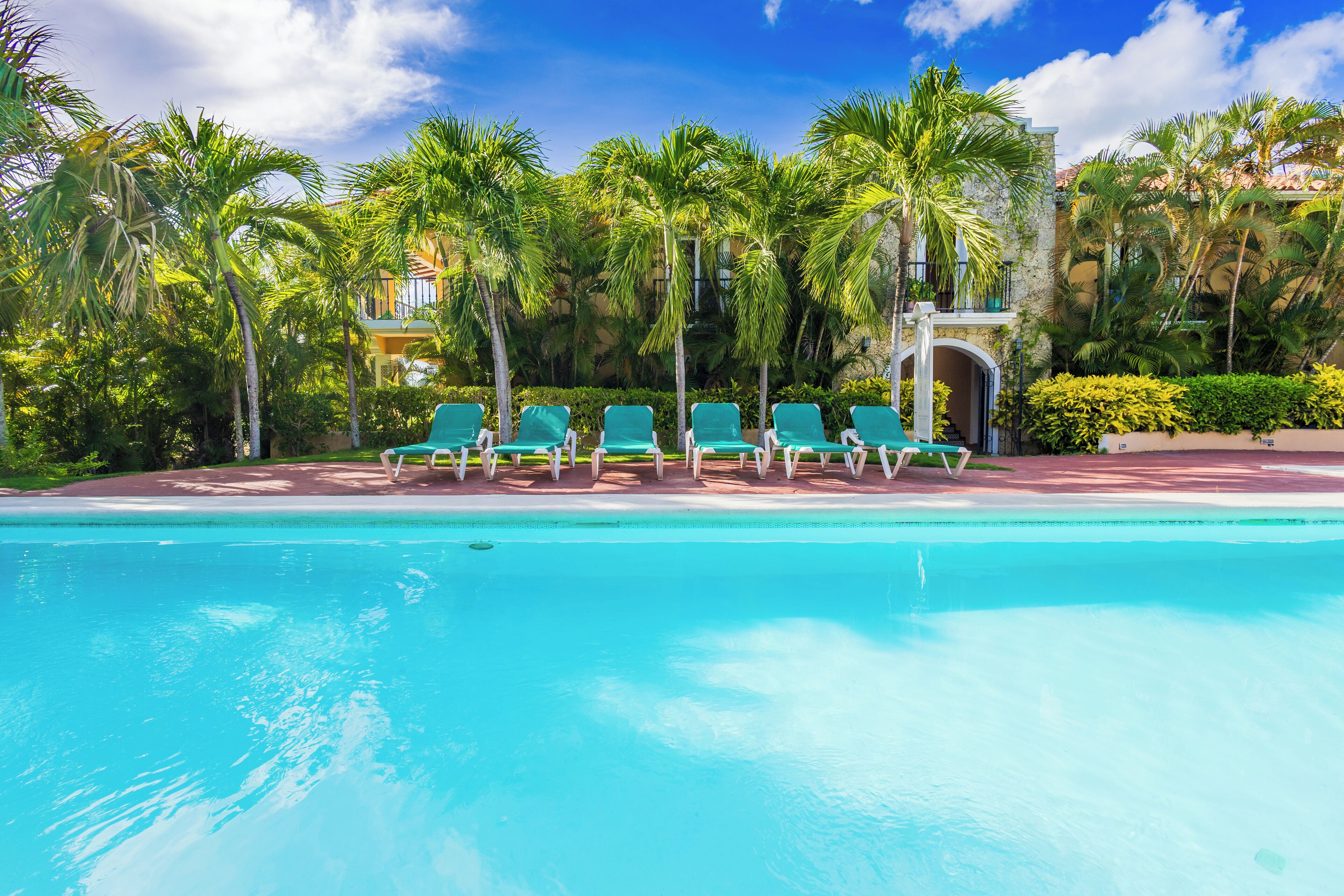 A pool with clear blue water, surrounded by green lounge chairs and palm trees.