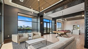 Un salon moderne doté d’une table de billard, de canapés et d’une grande fenêtre offrant une vue sur la ville.