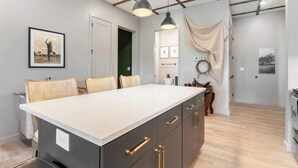 Une cuisine moderne dotée d’un grand îlot central, de meubles de rangement aux couleurs sombres et de luminaires suspendus.