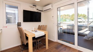 Une pièce comprenant une table en bois, deux chaises, un téléviseur à écran plat et un appareil de climatisation.