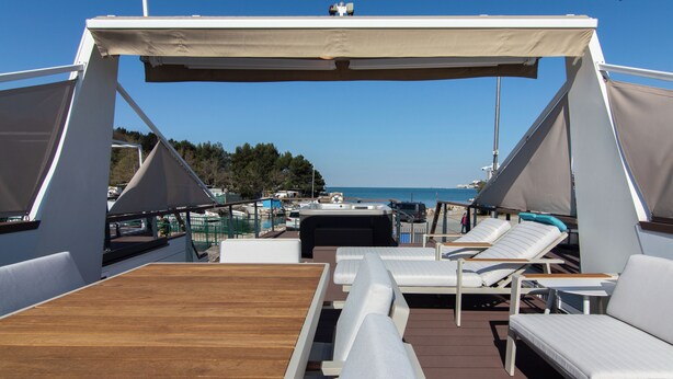 Une terrasse dotée de chaises longues et d’une table en bois, offrant une vue sur une marina et la mer.