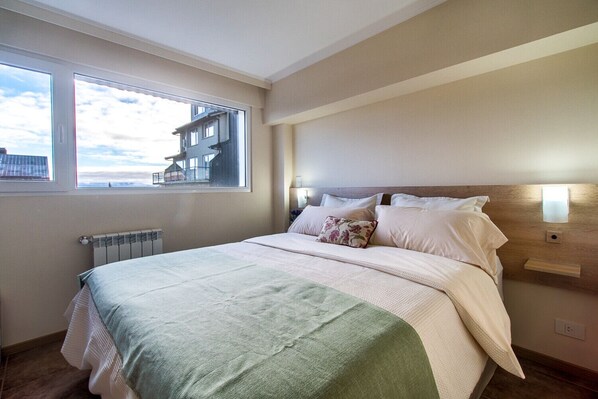 Relax in this serene bedroom with a large bed and a window offering a view of the surrounding building.