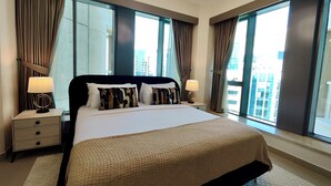 Une chambre d’hôtel moderne avec un grand lit, deux tables de chevet, une lampe et une vue sur la ville grâce à de grandes fenêtres.