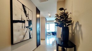 Un couloir orné d’œuvres d’art abstraites, une plante en pot posée sur une console, et une vue sur un coin repas avec des chaises et une table.