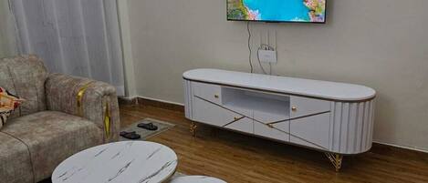 A living room with a sofa, two round coffee tables, a white entertainment unit, and a flat-screen TV mounted on the wall.