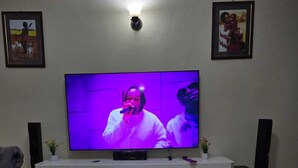 A living room with a flat-screen TV mounted on the wall, a glass coffee table, and a sofa. - Lux Suites Astrol Apartments Garden City (Nairobi)