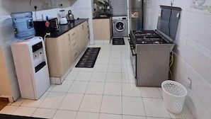 A compact kitchen with white cabinets, a water dispenser, a stove, and a washing machine. - Lux Suites Astrol Apartments Garden City (Nairobi)