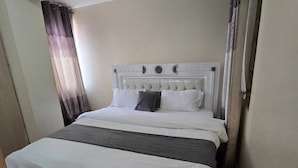 A single bed with a white headboard, a grey blanket, and a white duvet. - Lux Suites Astrol Apartments Garden City (Nairobi)