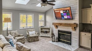 A living room with a fireplace, a ceiling fan, and a flat-screen TV mounted on the wall. - New! Large 2 Bedroom Kelleys Island Condo (Kelleys Island)