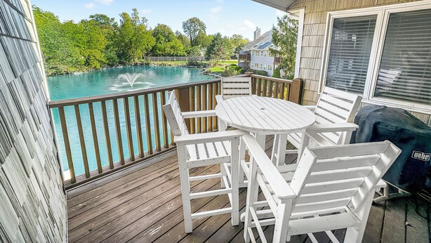 A wooden deck with a white table and chairs, overlooking a swimming pool and lush greenery. - New! Large 2 Bedroom Kelleys Island Condo (Kelleys Island)