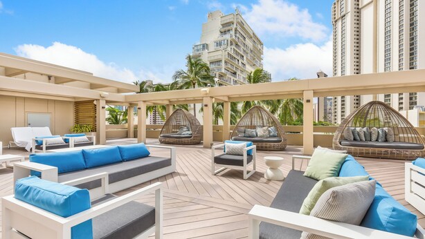 A rooftop lounge area with multiple seating options including sofas and chairs, a pergola structure, and a view of tall buildings in the background. - Ocean Views + Walkway to Mall-Ala Moana Hotel 2513 (Honolulu)