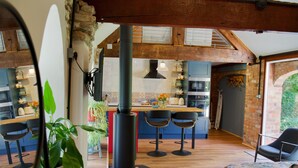 A modern kitchen with wooden beams, a central island, bar stools, and a decorative plant.