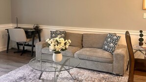 Ein Wohnzimmer mit grauem Sofa, einem Glastisch und einem Essbereich mit schwarzem Tisch und Stühlen.